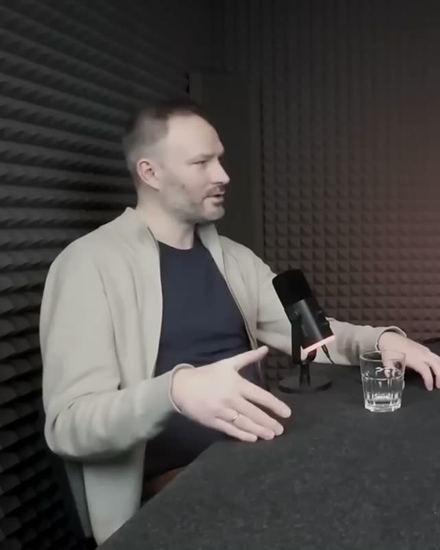 Marcin Sobczyk w beżowym swetrze mówi i gestykuluje przy mikrofonie.